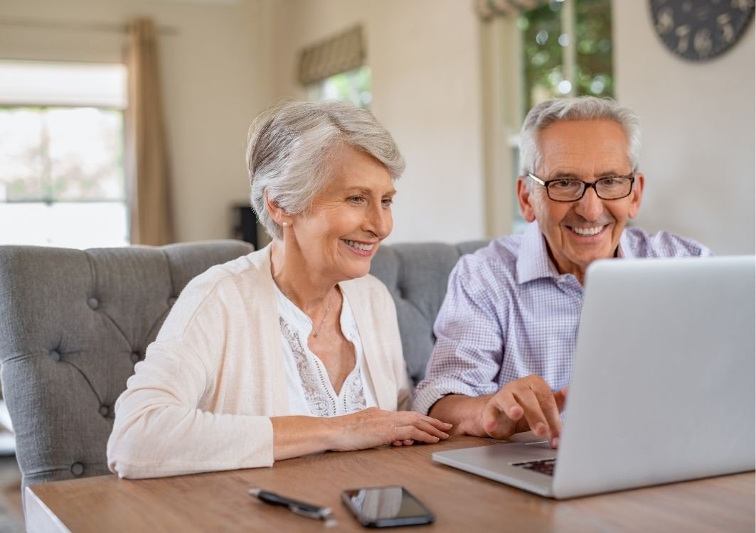 Two seniors sitting at dining room table typing on laptop